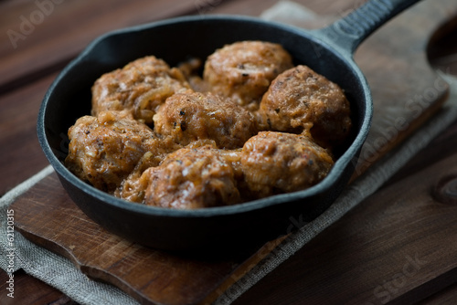 Meatballs with gravy in a frying pan, rustic wooden background