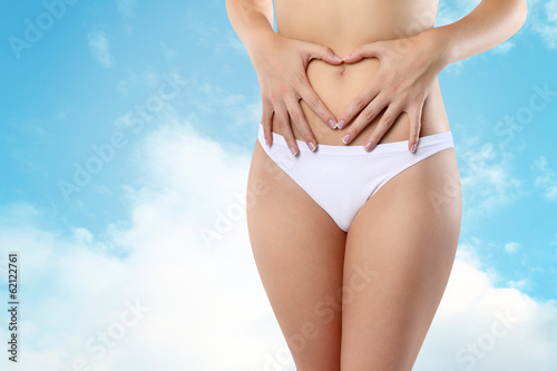 Woman s hands on stomach on sky background wellness concept
