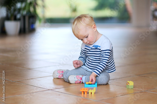 Cute little baby girl play with plastic bricks sitting indoors o
