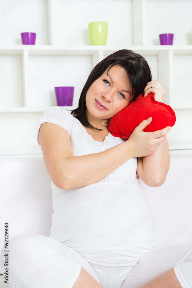 Beautiful pregnant woman smiling and holding heart shape pillow Beautiful pregnant woman smiling and holding heart shape pillow