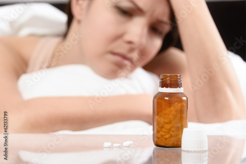 Frau im Bett betrachtet eine Flasche Tabletten