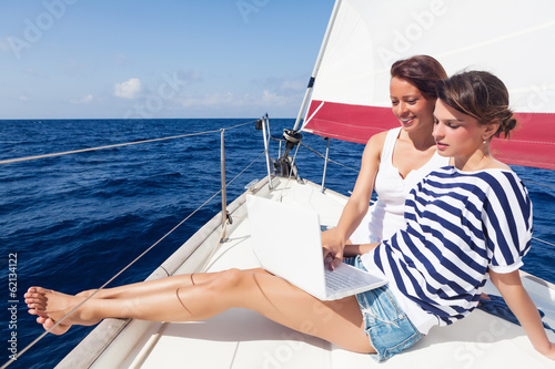 Happy women on the bow of a Sailboat using a laptop,Copy space