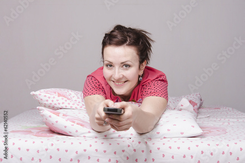 девушка с пультом лежит в постели и улыбается
