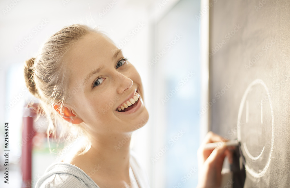 beautiful young woman drawing a smiley face on a blackboard at h