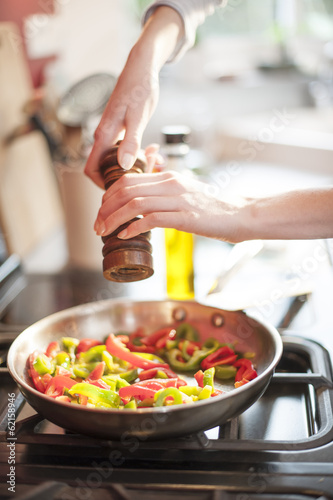 Closeup on hands turning a pepper mill in a pan