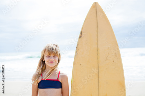 Smiling young girl standing next to surfboard