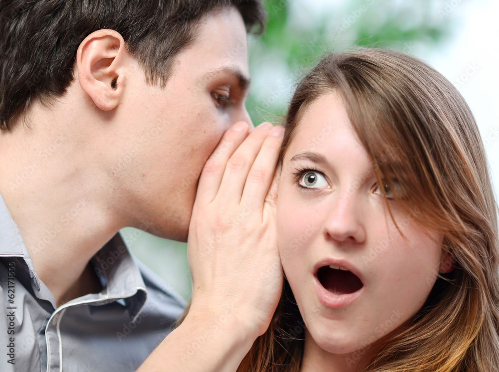man whispering in the ear of his surprised wife man whispering in the ear of his surprised wife