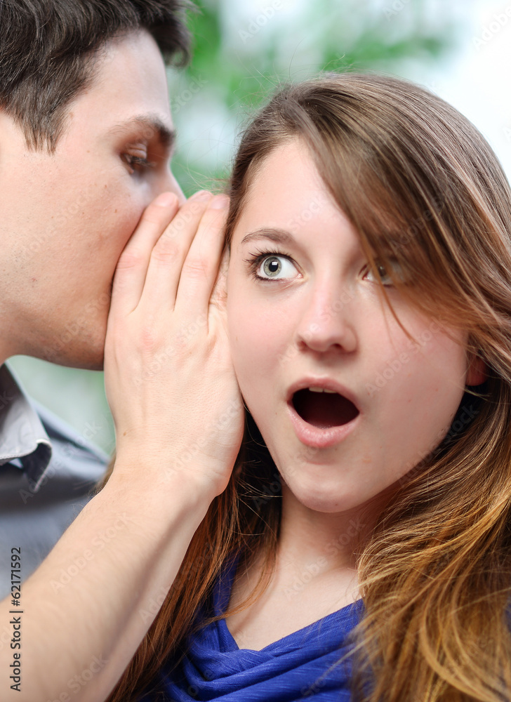 man whispering in the ear of his surprised wife man whispering in the ear of his surprised wife