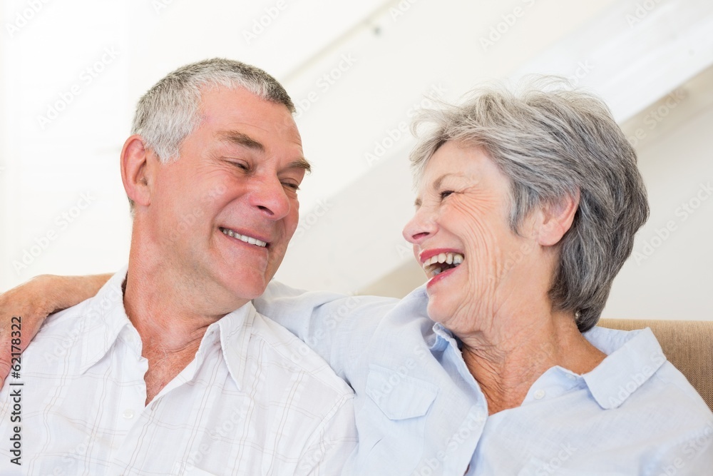Retired couple sitting on couch smiling at each other Retired couple sitting on couch smiling at each other