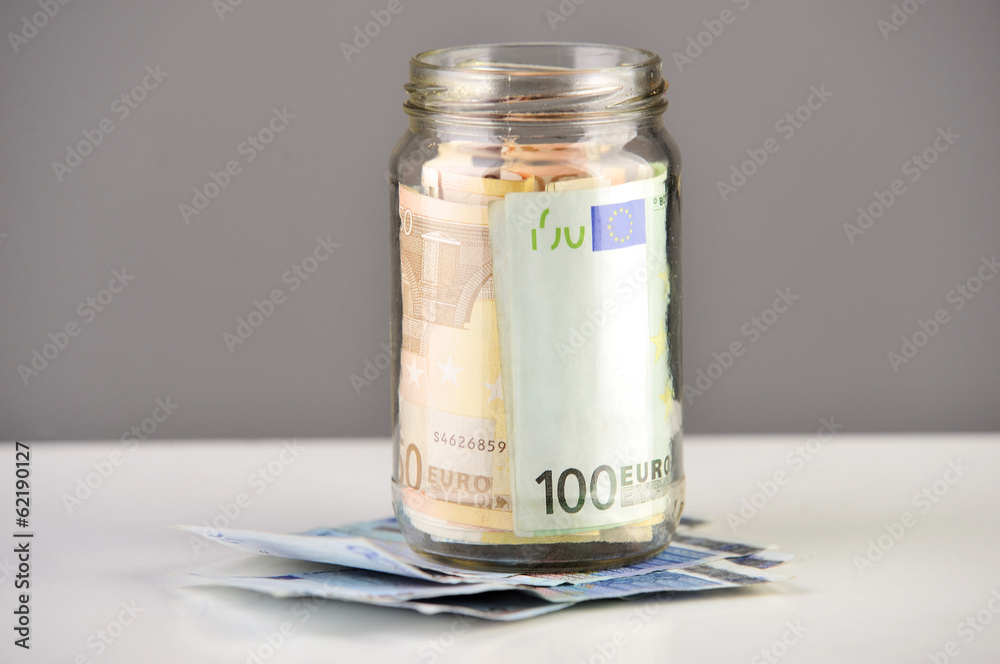 Roll of euro banknotes in a money jar against white background Roll of euro banknotes in a money jar against white background