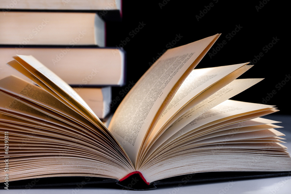 Naklejka premium Buch aufgeschlagen vor Bücherstapel