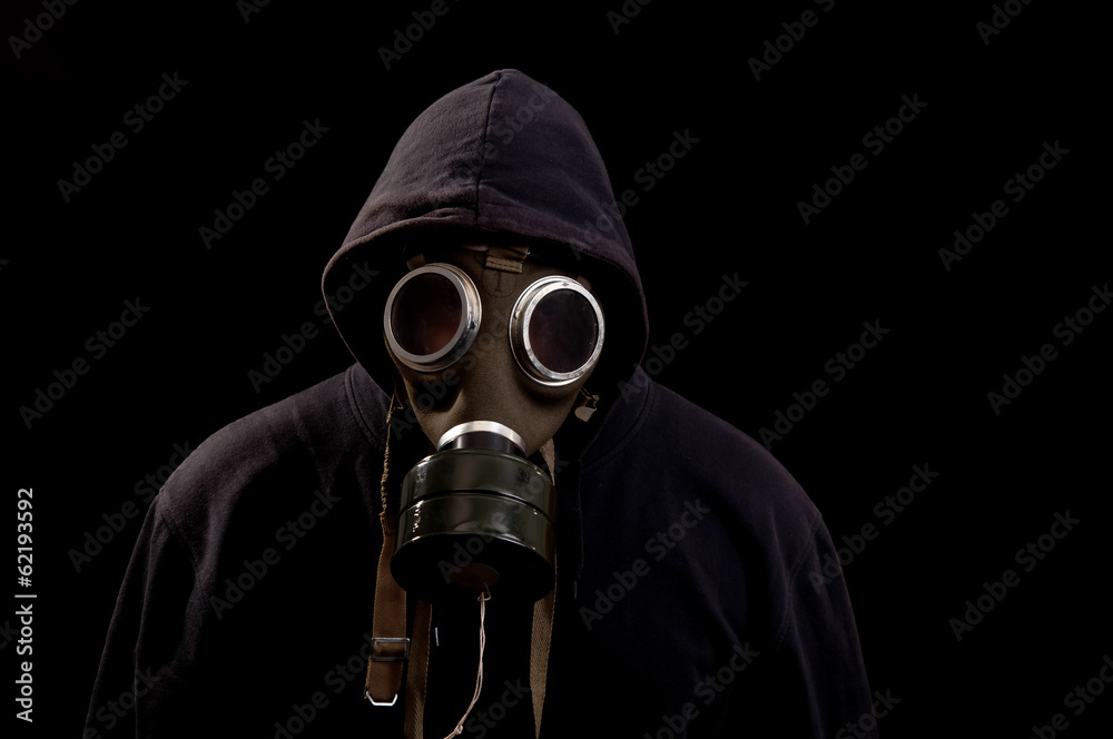 Man in black clothes wearing a classic gas mask over a dark back Man in black clothes wearing a classic gas mask over a dark back