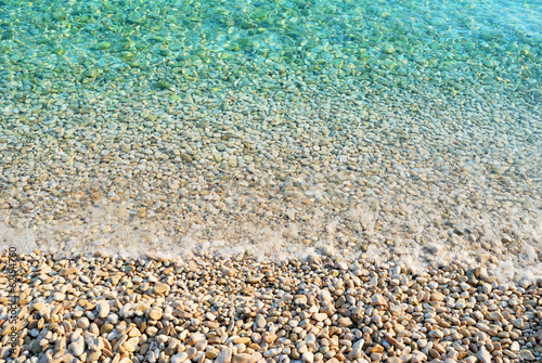 Pebble beach with azure sea water texture background