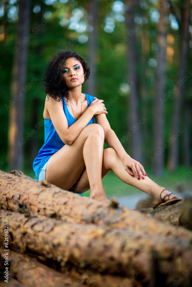 Obraz premium Beautiful Young Woman sitting on log posing