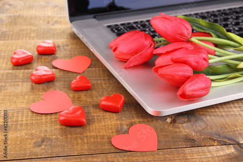 Fototapeta Naklejka Na Ścianę i Meble -  Computer with red hearts and flowers on table close up