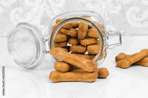 Homemade dog biscuits spilling from a glass canister.