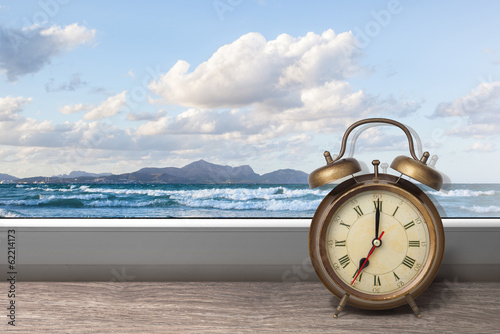 View of summer sea under blue sky from window with alarm clock