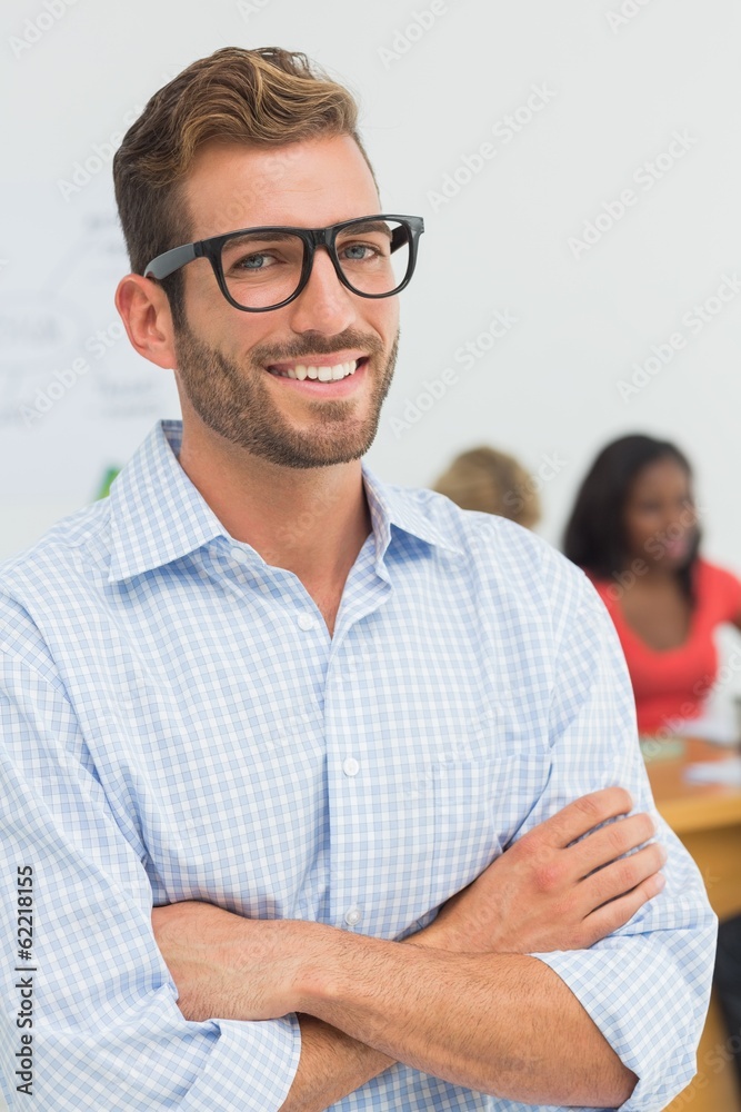 Fototapeta premium Attractive designer smiling at camera with colleagues behind him