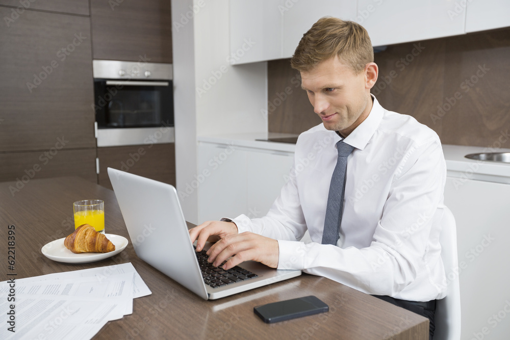Businessman using laptop at breakfast table Businessman using laptop at breakfast table