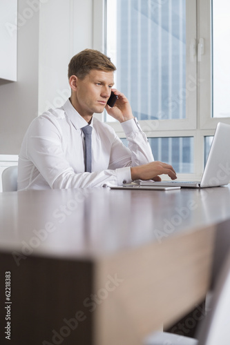 Mid adult businessman on call while using laptop at home