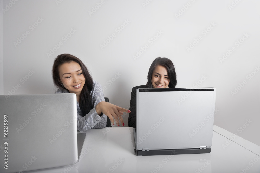 Smiling businesswomen using laptop at desk in office