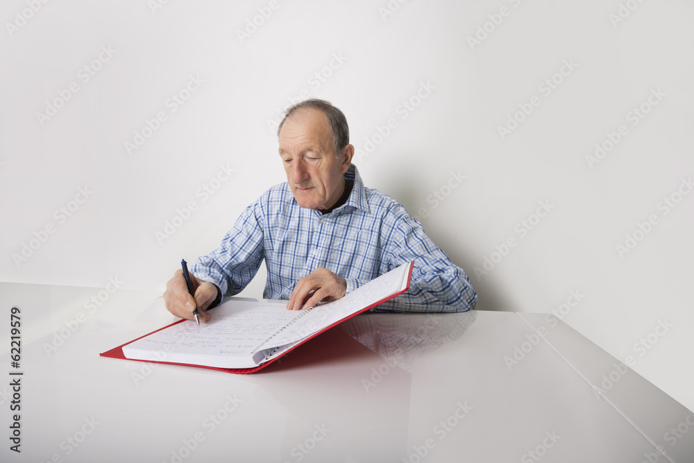 Senior businessman writing in file at desk Senior businessman writing in file at desk