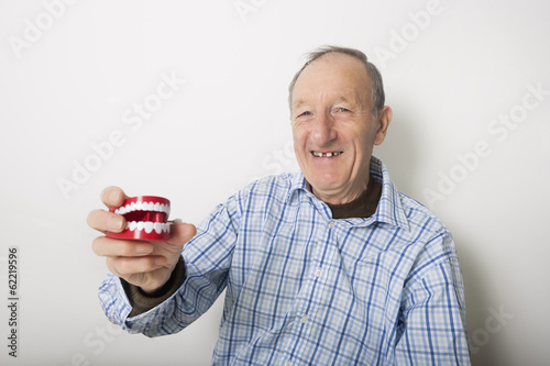 Portrait of smiling senior man holding teeth model against gray background