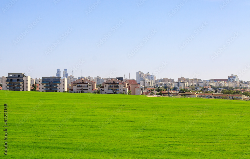 Beer Sheva suburb behind a green field under blue sky