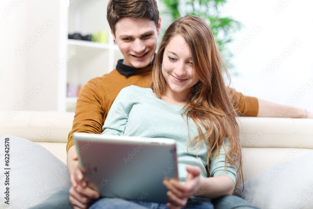 Young couple using digital tablet indoors on the sofa Young couple using digital tablet indoors on the sofa