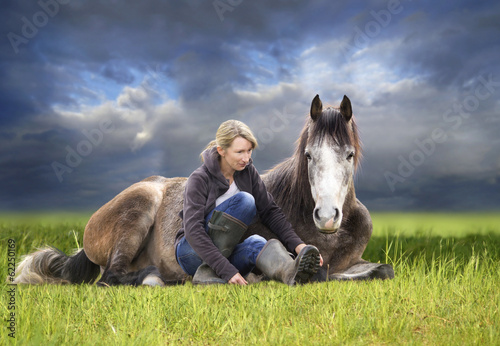 horse and woman lying in green field against sky after storm