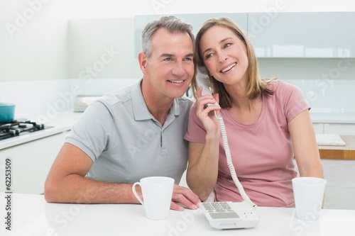 Happy couple using landline phone together in kitchen