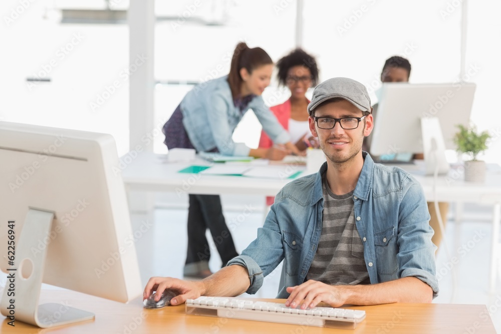 Casual male artist using computer with colleagues in background Casual male artist using computer with colleagues in background