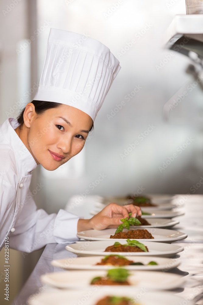Smiling female chef garnishing food in kitchen Smiling female chef garnishing food in kitchen