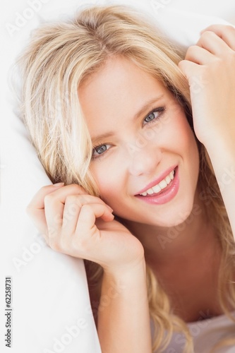 Pretty young blonde smiling at camera from under the sheet