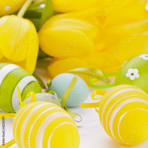 Farbenfrohe gelbe Tulpen mit grünen Blättern und Ostereiern zu photo