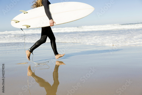 Photography Teenage girl running on the beach with her surfboard