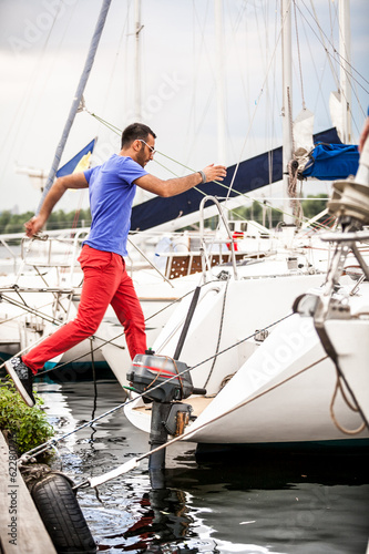 Handsome latin man jumping on yacht from pier