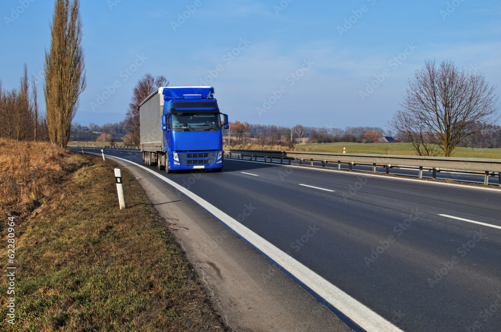Rural landscape with an asphalt highway and blue truck
