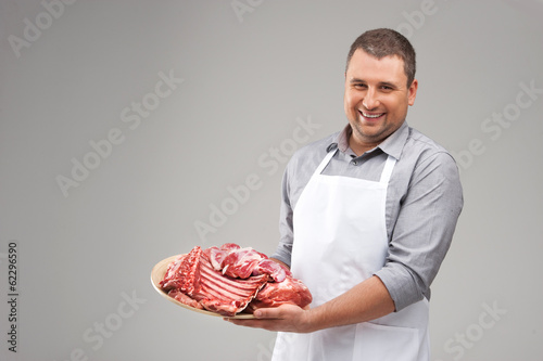 professional butcher smiling and holding raw meat.