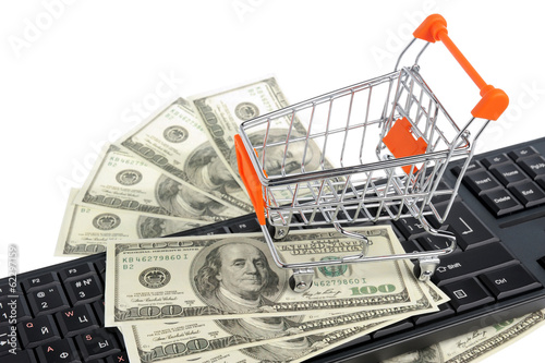 Shopping cart with money on black keyboard isolated on white