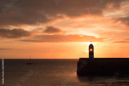 Lighthouse on breakwater wall with calm sea during sunrise