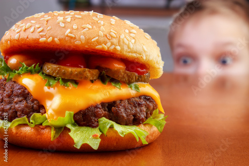 Hungry young boy is staring beef burger on table photo