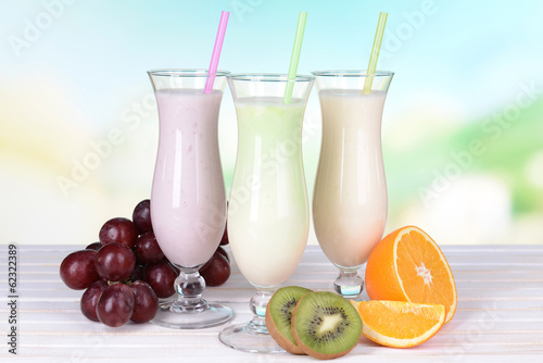 Milk shakes with fruits on table on light blue background