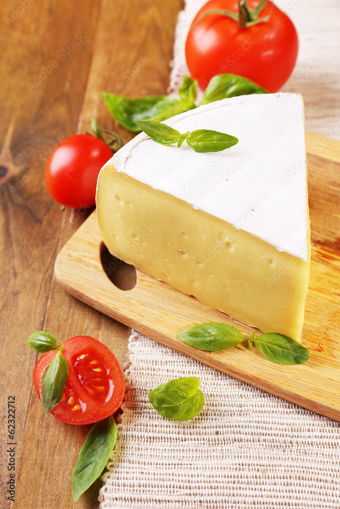 Tasty Camembert cheese with tomatoes and basil, on wooden table Tasty Camembert cheese with tomatoes and basil, on wooden table