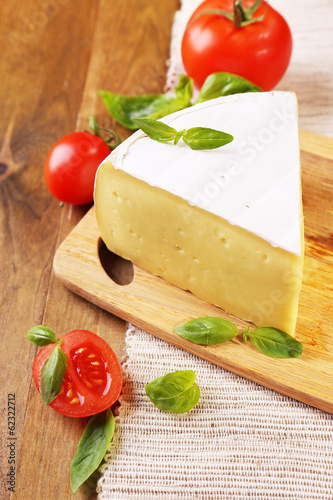 Tasty Camembert cheese with tomatoes and basil, on wooden table