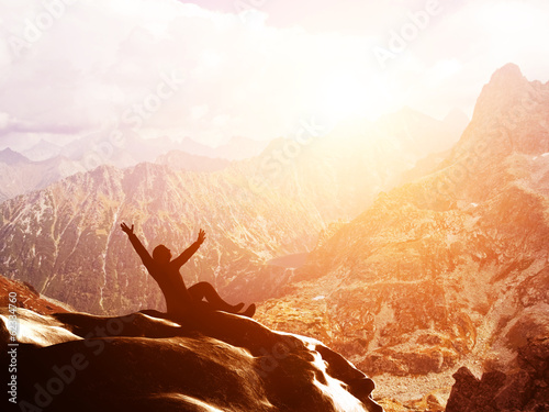 A happy man sitting on the peak of a mountain with hands raised