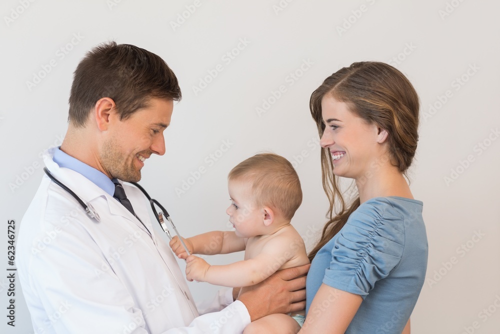 Handsome pediatrician checking baby boy held by his mother Handsome pediatrician checking baby boy held by his mother