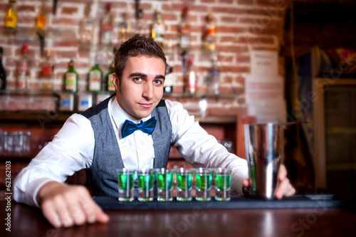 portrait of young male barman behind the bar with alcoholic shot