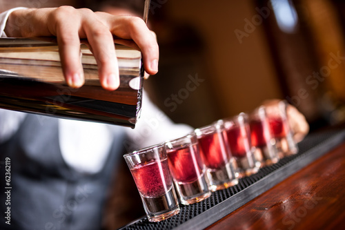 Slika na platnu close-up of barman hand pouring alcohol into shot glasses