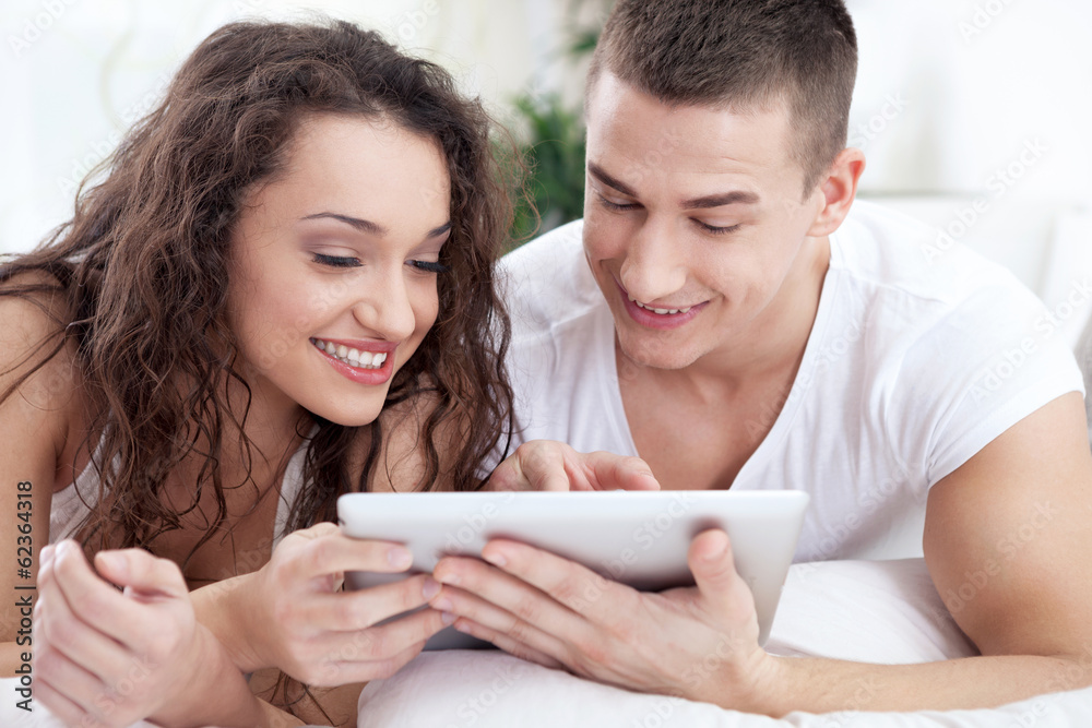 Young couple sitting on the bed using tablet pc Young couple sitting on the bed using tablet pc